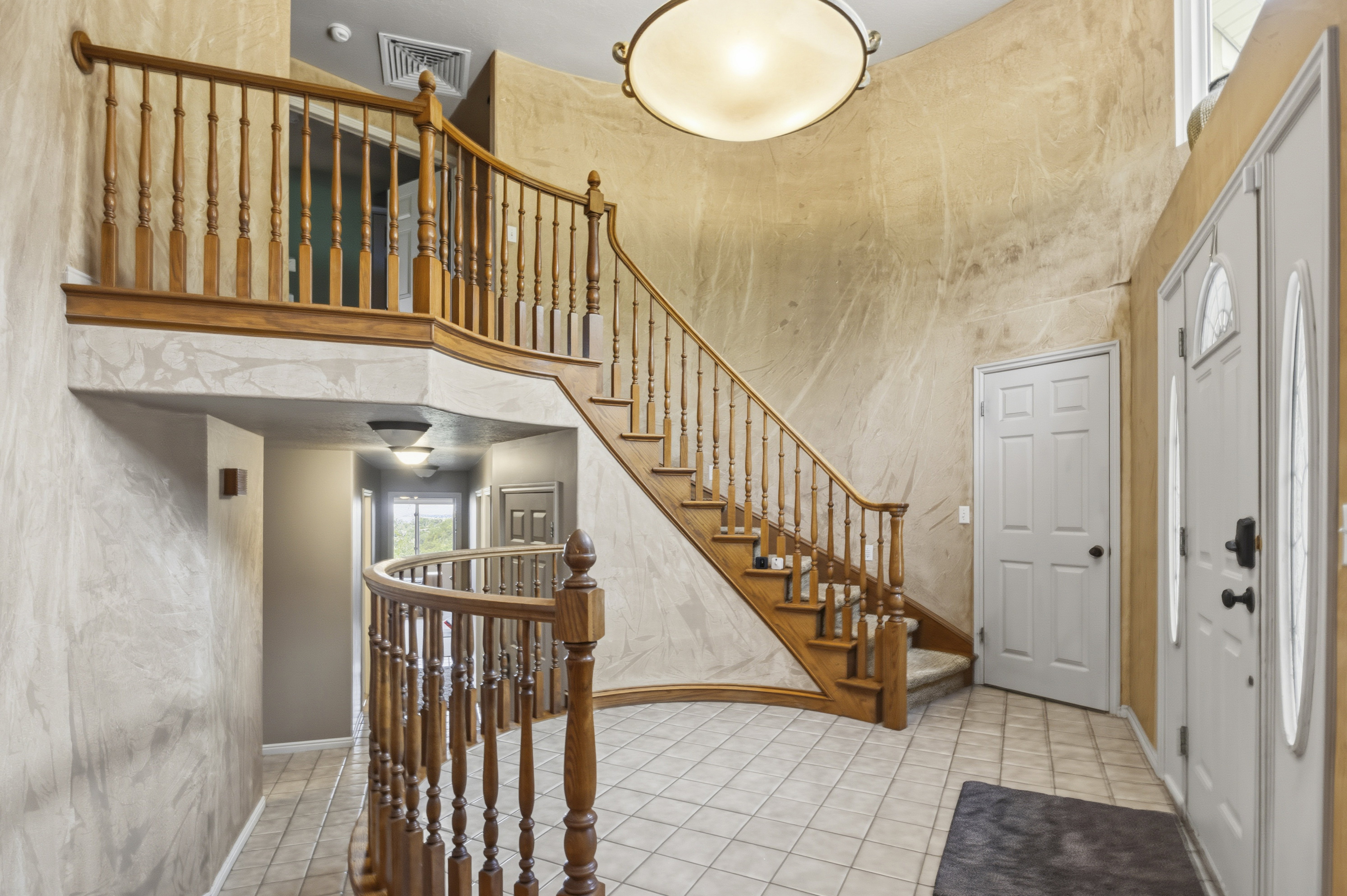 Grand foyer featuring a curved staircase with wood balusters, tile flooring, and a decorative overhead light fixture