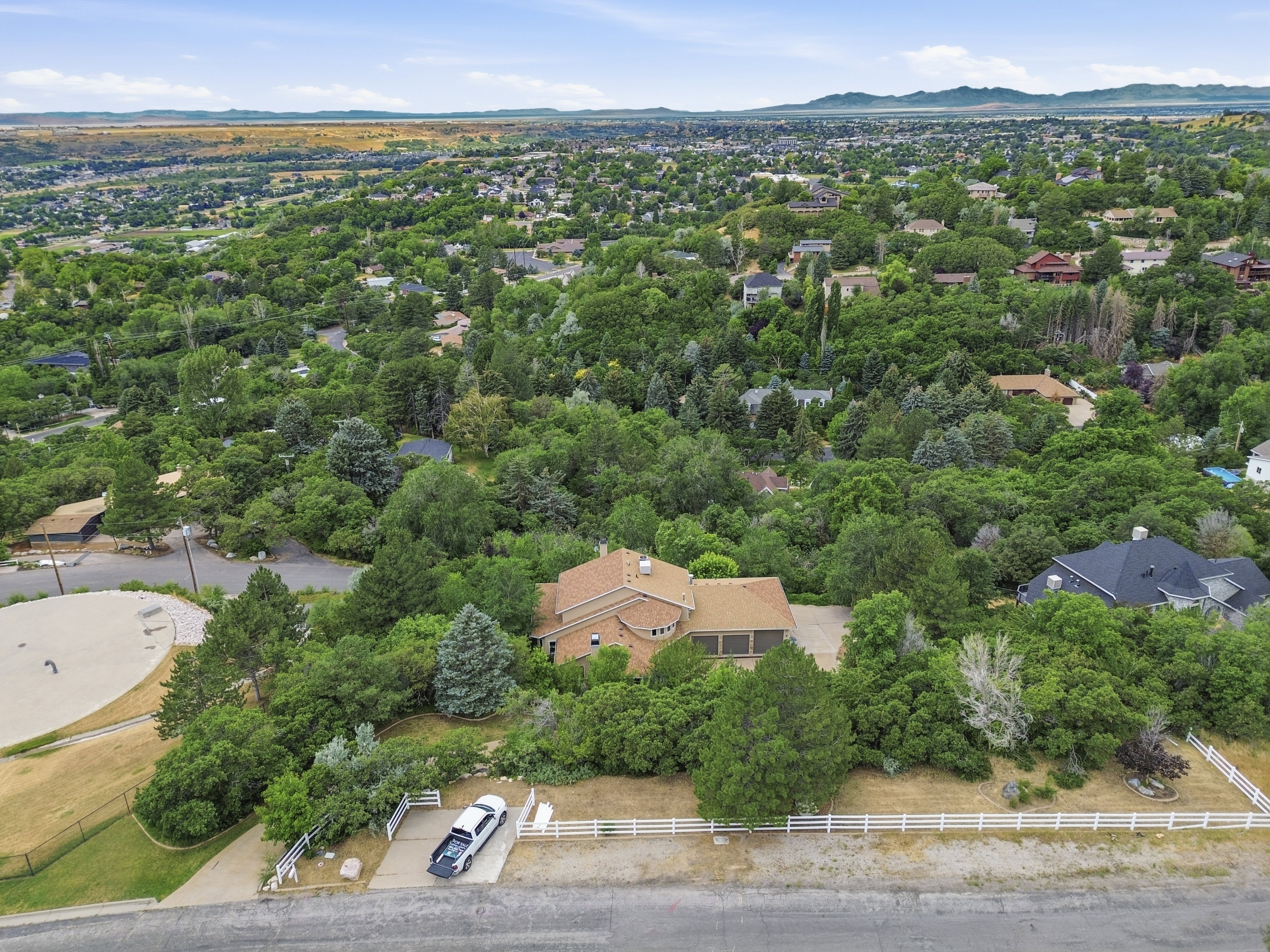 Brick exterior residence with a multi-car garage, mature landscaping, and white fencing bordering the property
