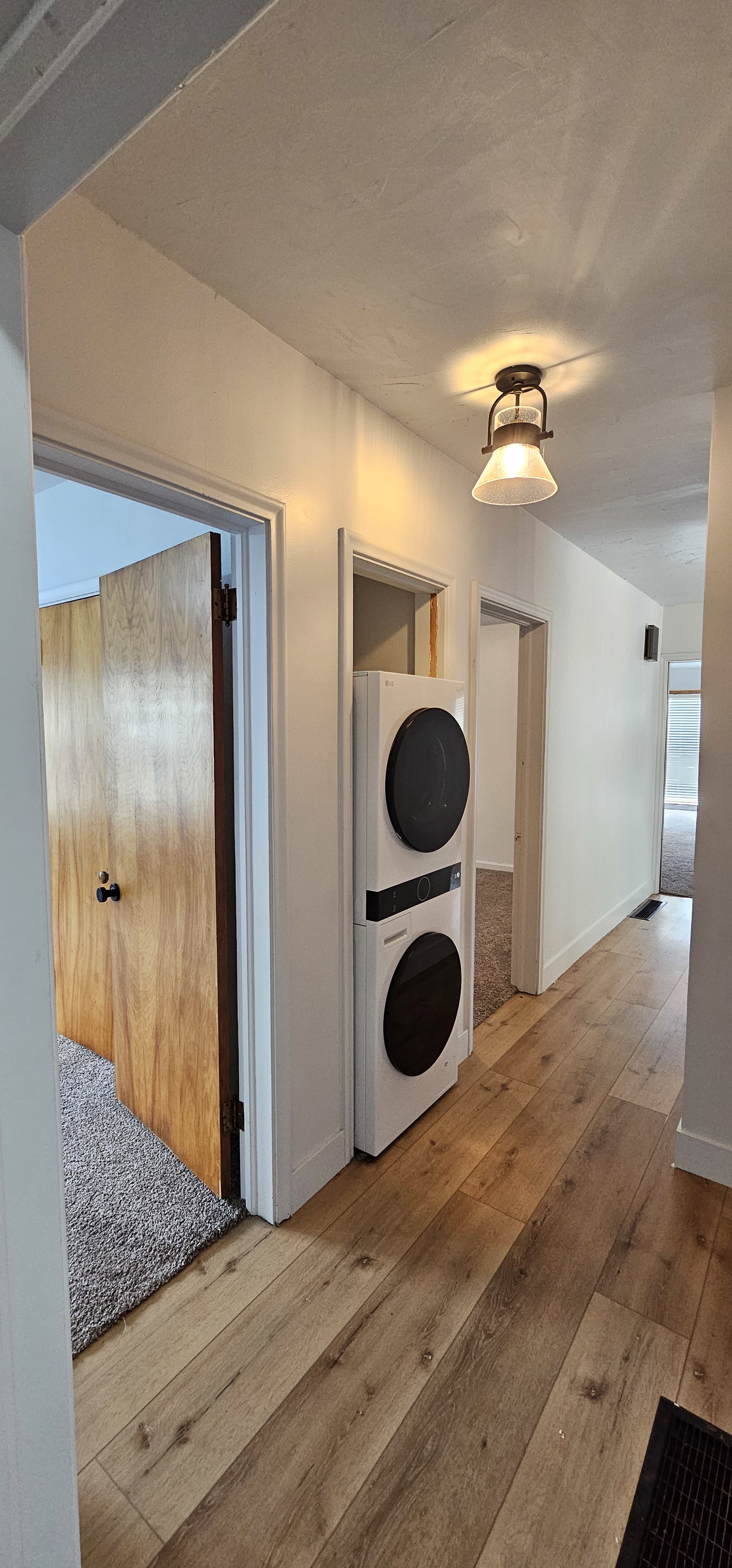 Hallway featuring wood-finish flooring, white walls, and a built-in stacked washer and dryer unit