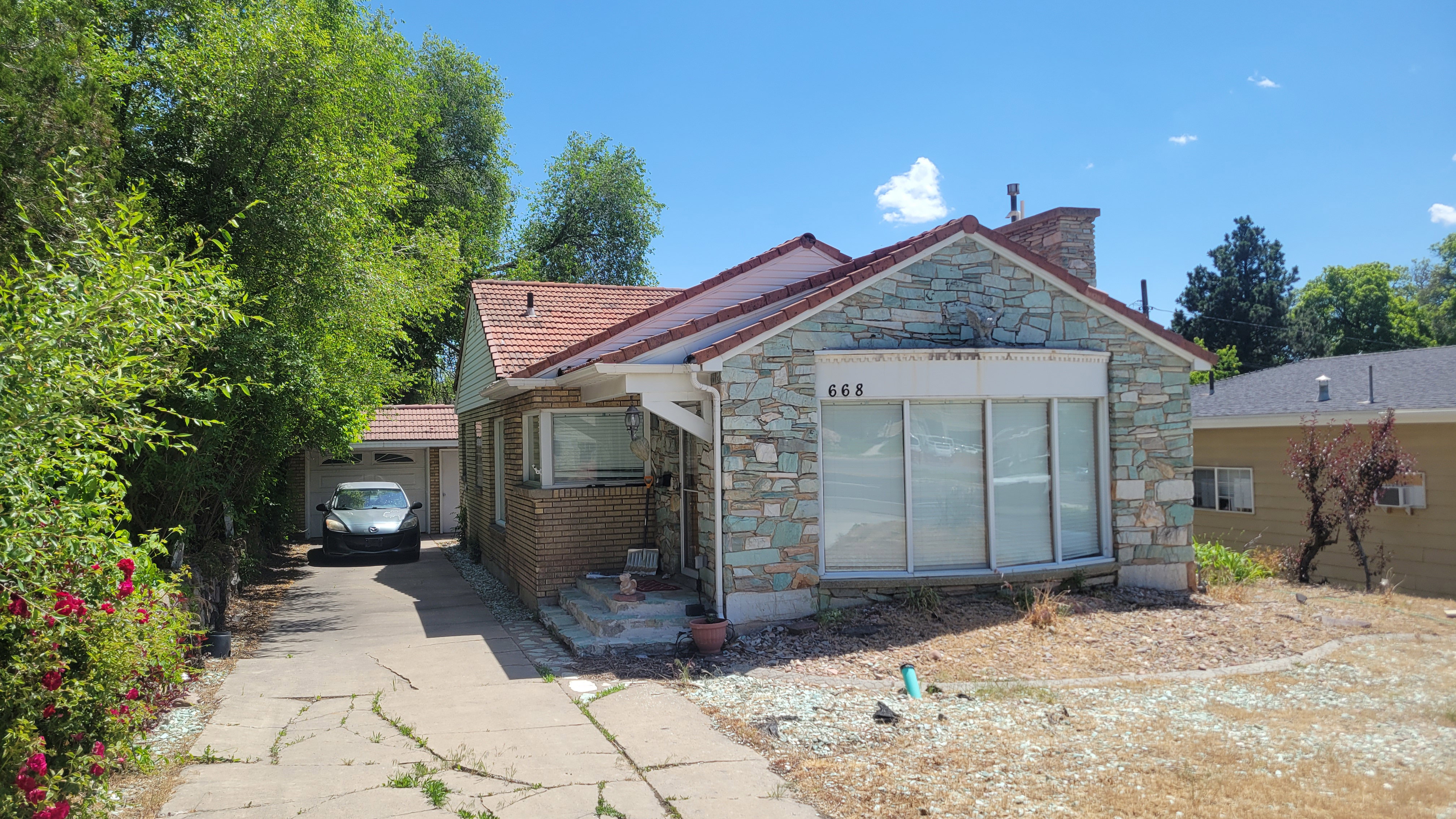 Exterior featuring a red tile roof, stone facade, brick siding, an attached covered porch, and a paved driveway leading to a detached garage