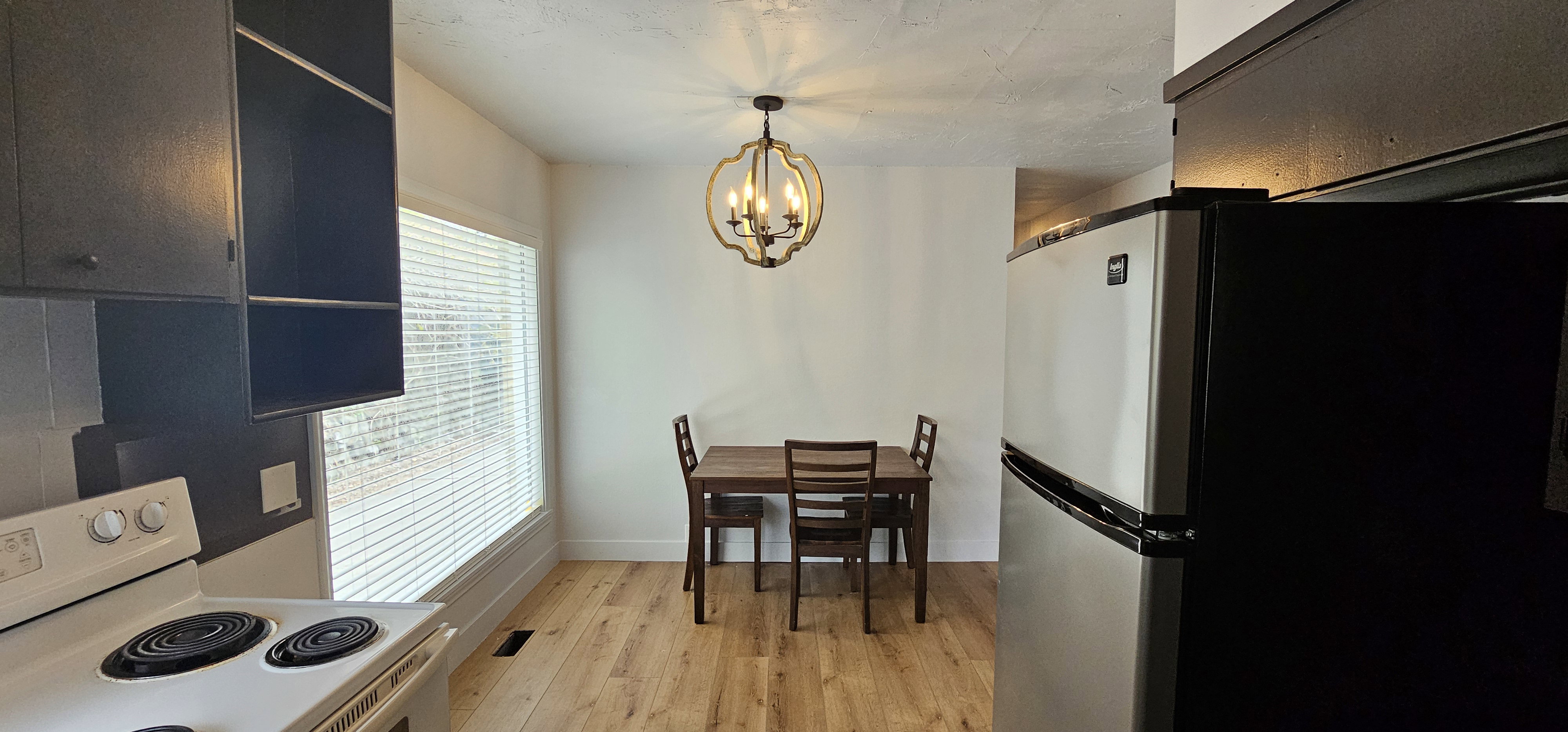 Dining area featuring wood-finish flooring, a contemporary chandelier, and a large window with blinds