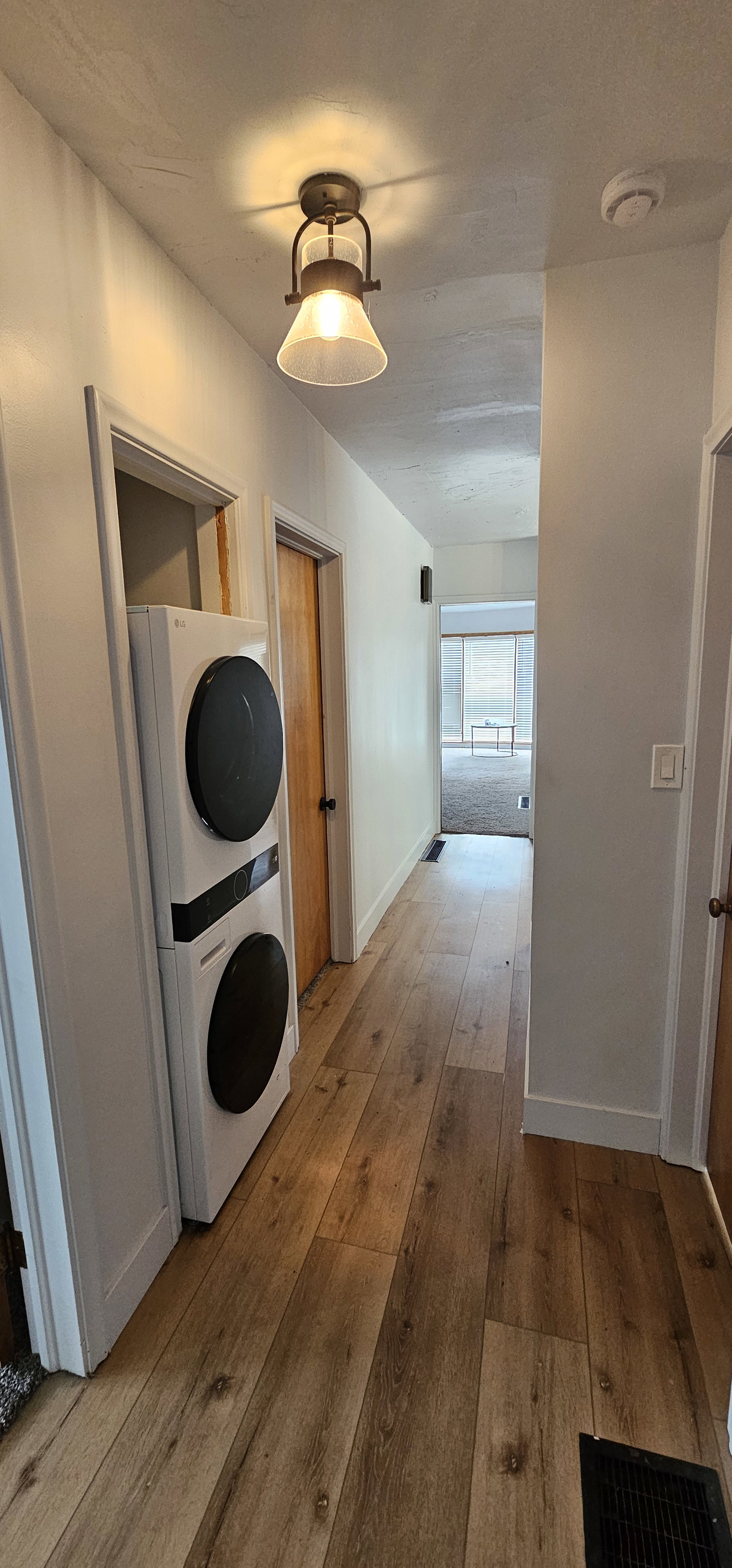 Hallway featuring wood-finish flooring, white walls, and a stacked laundry unit