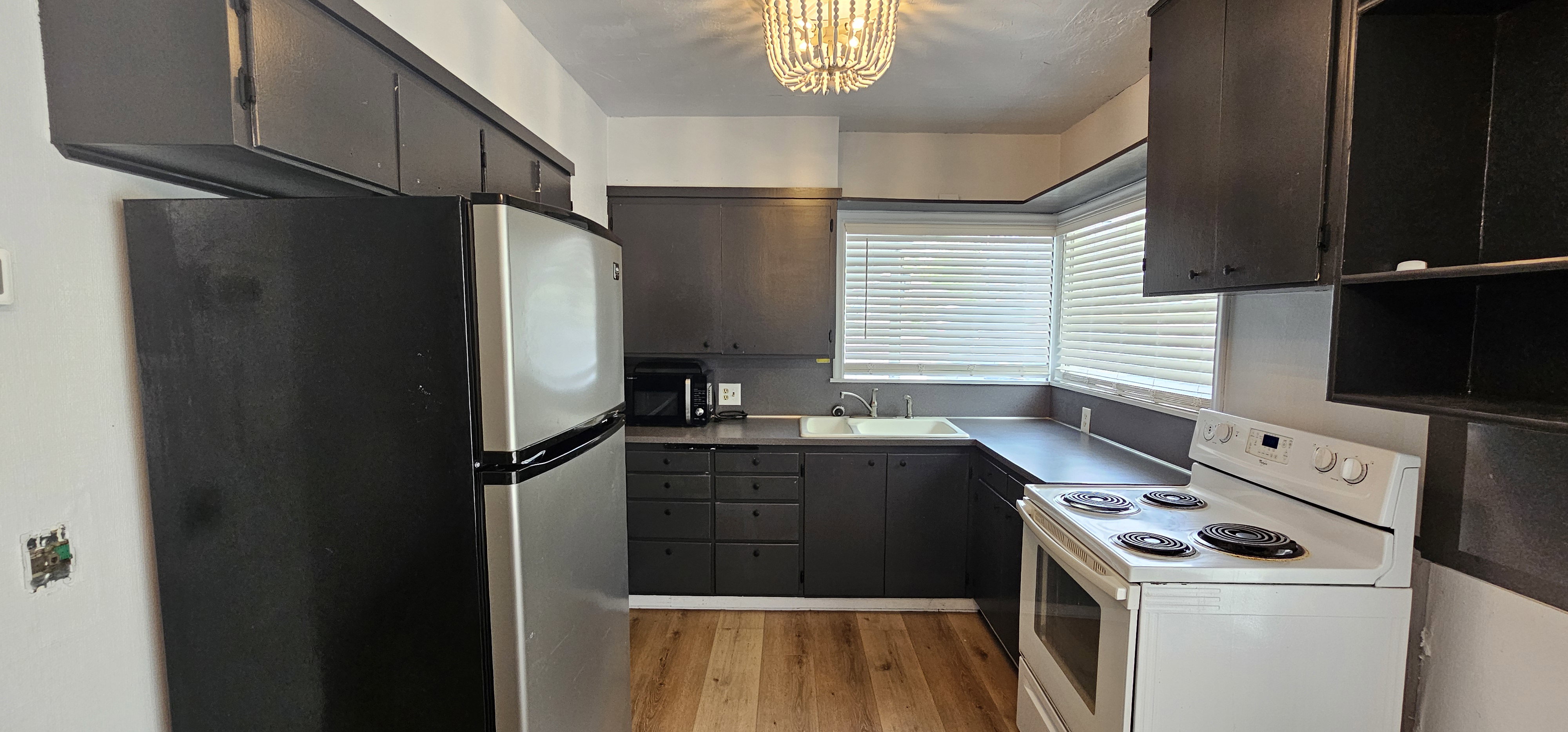 Kitchen featuring wood-finish flooring, dark cabinetry, and a corner window with horizontal blinds