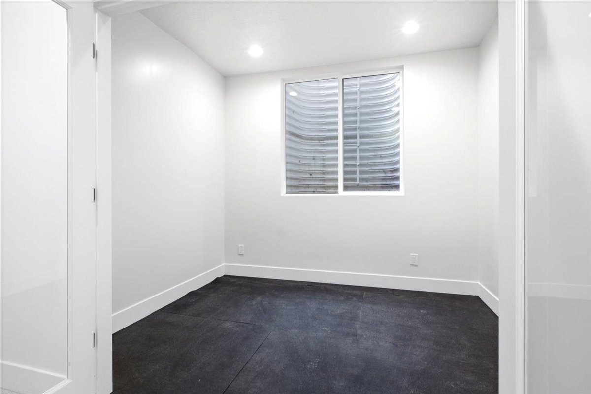 Room with clean white walls and dark flooring, featuring a window with a window well