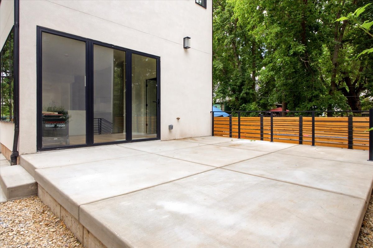 Expansive concrete patio featuring a modern horizontal slatted wood fence with dark metal posts, and large multi-panel glass doors