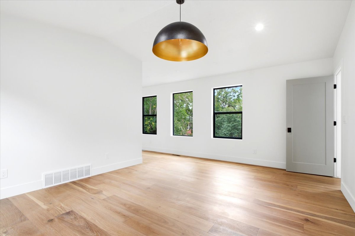 Spacious room with wood-finish flooring, white walls, and a modern dome pendant light