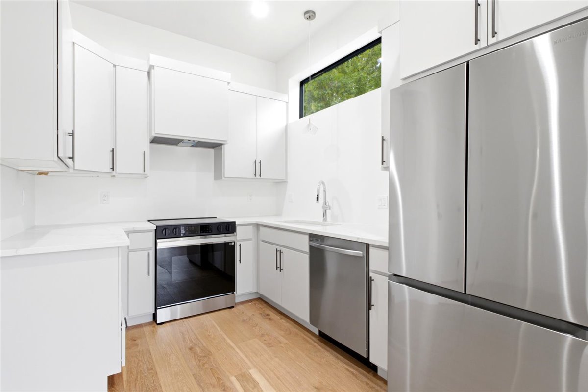 Modern kitchen featuring white cabinetry, stainless steel appliances, light wood-finish flooring, white countertops, and a horizontal window