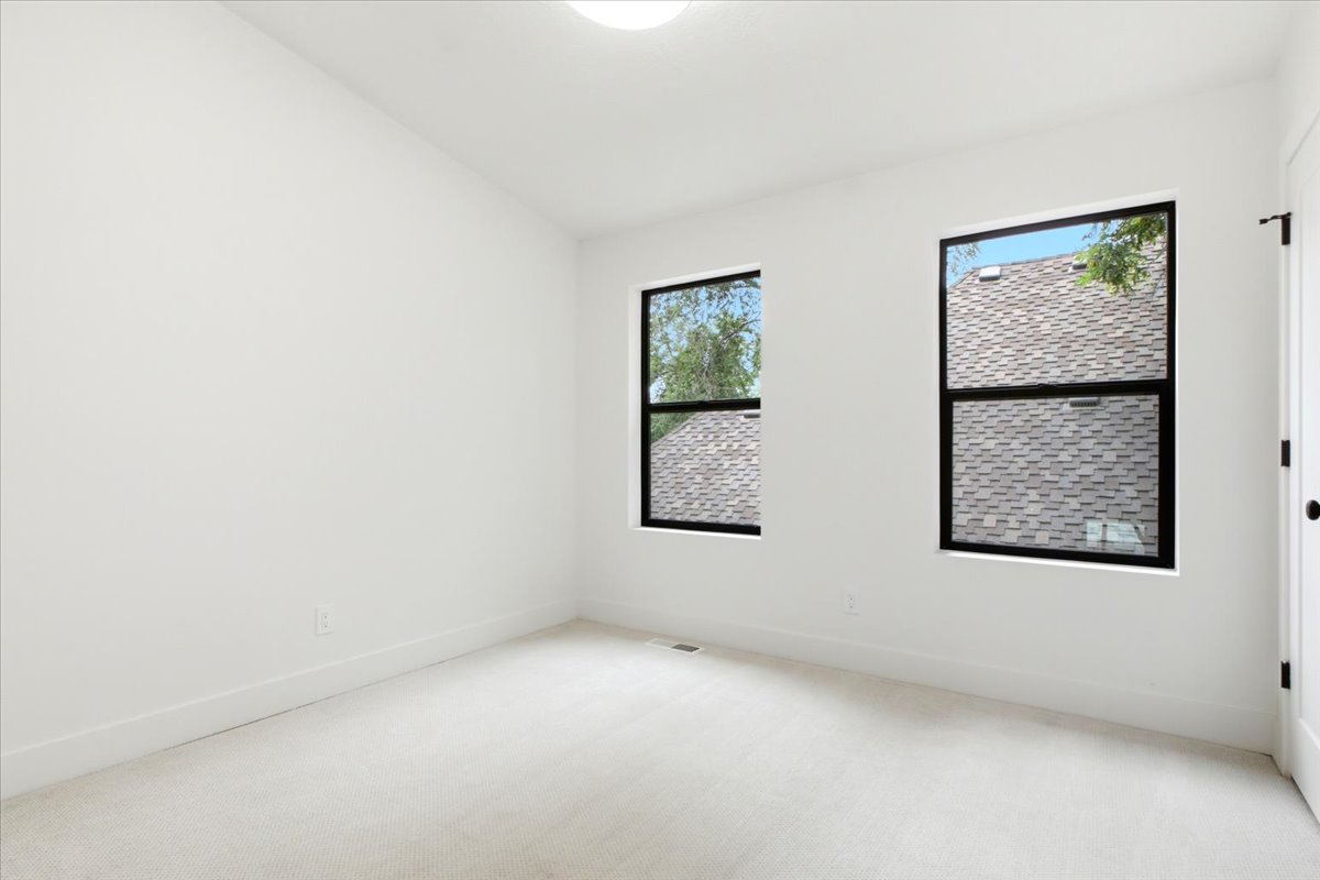 Bright room featuring two large windows with black frames, white walls, white trim, light-colored carpeting, and a flush-mount ceiling light