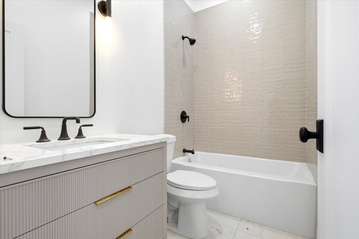 Bathroom featuring a white bathtub, a tiled shower surround, a white toilet, a vanity with a white countertop, and a rectangular mirror
