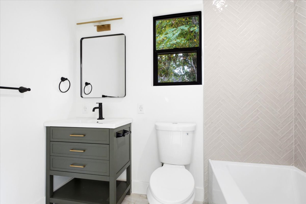 Bathroom featuring a contemporary dark green vanity with brass hardware, a rectangular framed mirror with an overhead brass light fixture, and a white countertop with an integrated sink