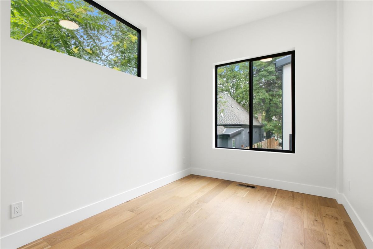 Room featuring wood-finish flooring, white walls, and a large window with black trim