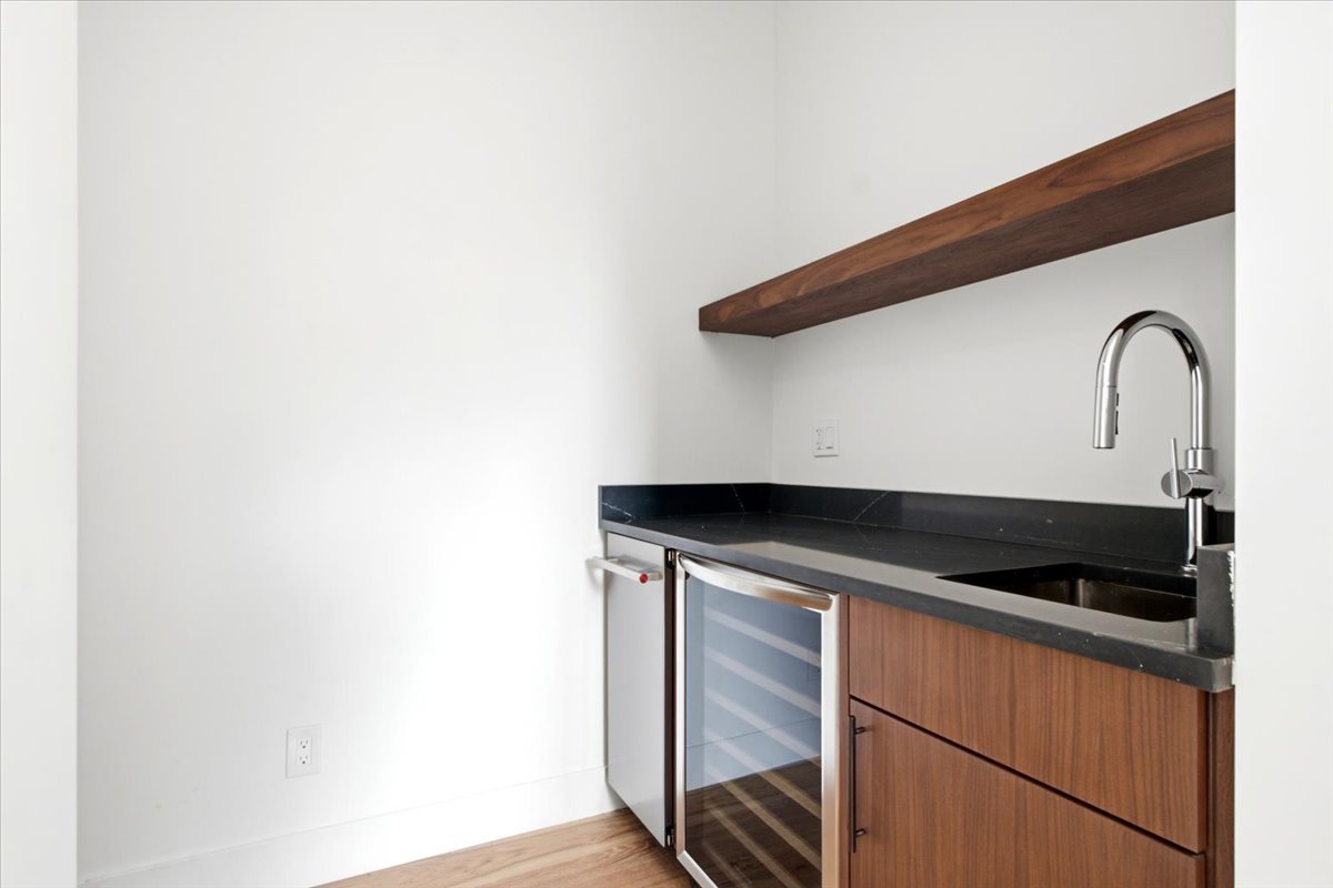 Wet bar featuring a dark stone countertop, wood-finish cabinetry, under-counter beverage cooler, and a floating wood-finish shelf