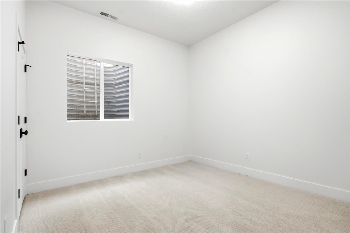 Carpeted room featuring a white window frame with a window well, white walls, and white baseboards