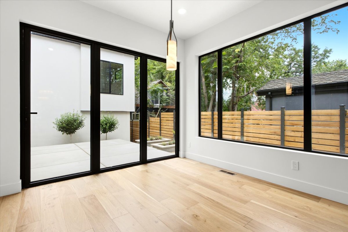 Spacious room featuring floor-to-ceiling windows, patio doors, light wood-finish flooring, and a contemporary pendant light fixture