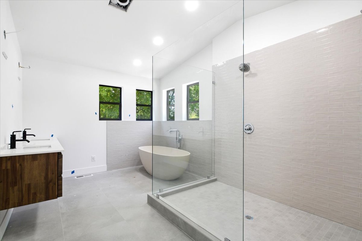 Contemporary bathroom featuring a frameless glass shower enclosure, a freestanding oval soaking tub, and a floating wood-finish vanity with dual undermount sinks and matte black fixtures