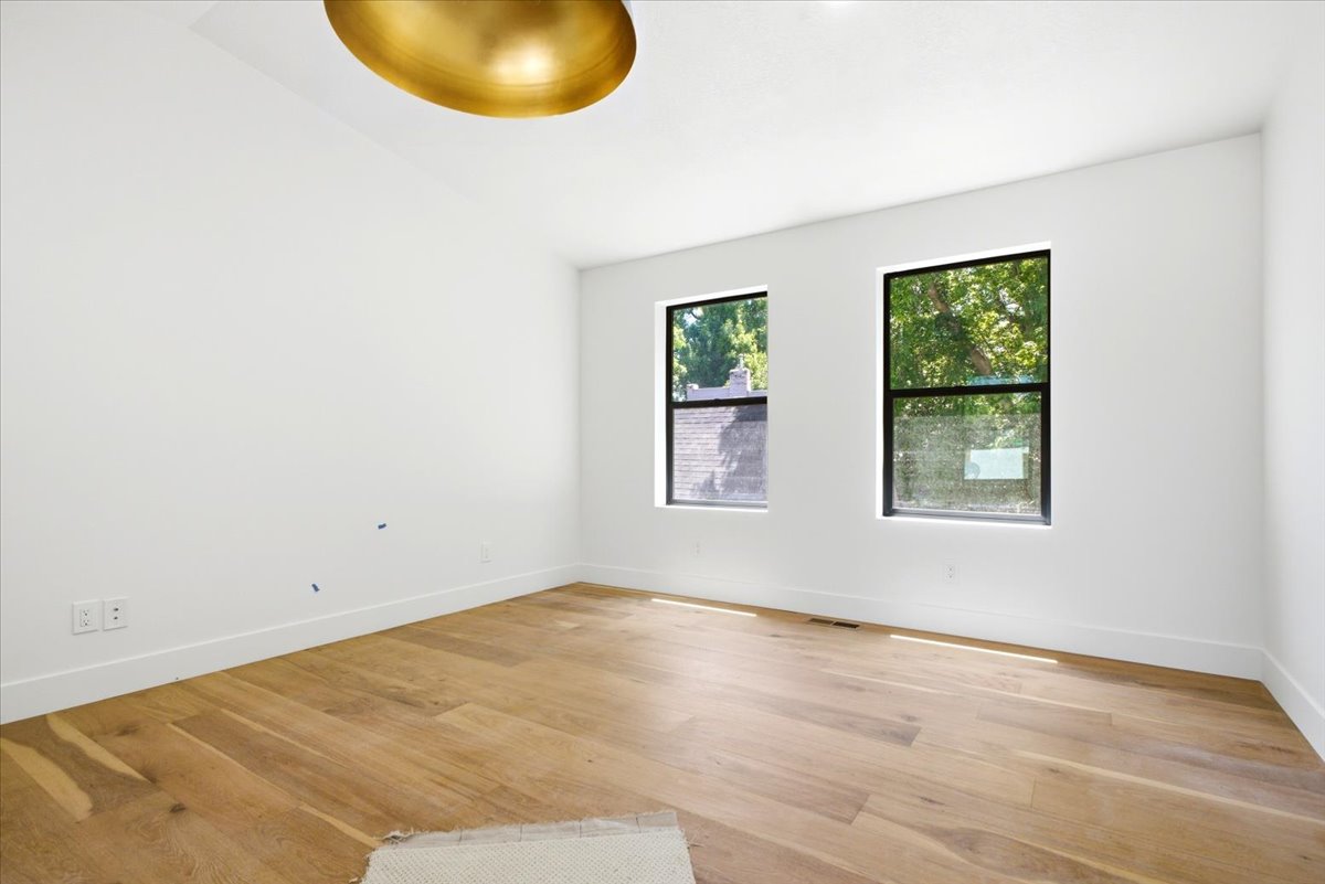Spacious room featuring light wood-finish flooring, crisp white walls, and a recessed gold-tone ceiling fixture