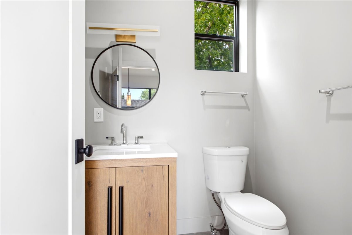 Powder room featuring a wood-finish vanity with a white countertop and undermount sink, a circular mirror, and modern wall-mounted lighting