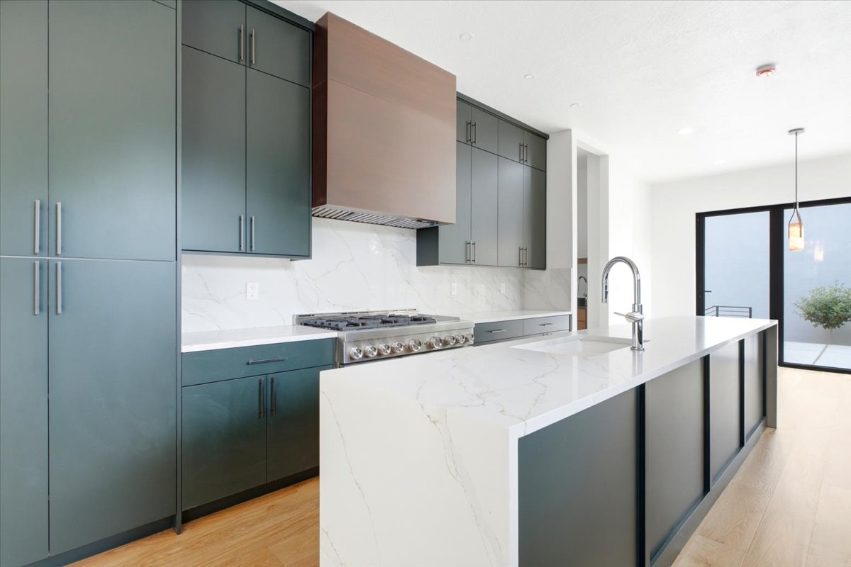 Modern kitchen featuring custom dark cabinetry, stone countertops with integrated sink, a large center island, and a professional-grade range