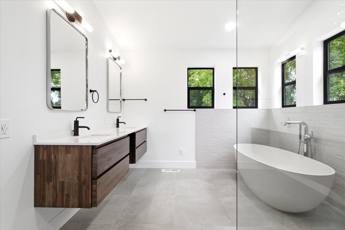 Primary Bathroom featuring a freestanding tub, dual floating wood-finish vanities with rectangular sinks and wall-mounted faucets, large rectangular mirrors, and light gray tile flooring