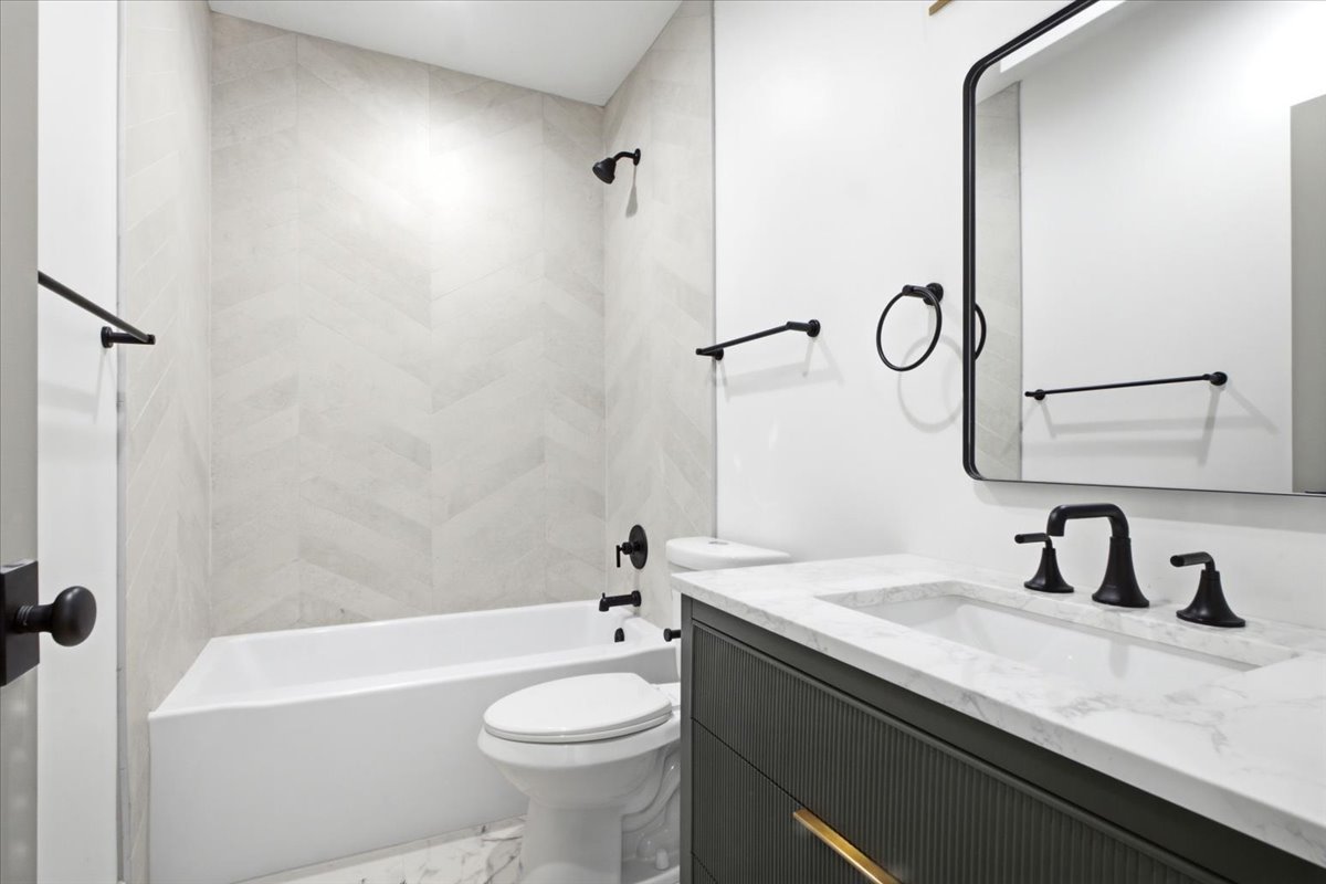 Bathroom featuring a white bathtub, herringbone pattern shower tile, dark gray vanity with fluted detailing, white countertop with integrated sink, and matte black fixtures