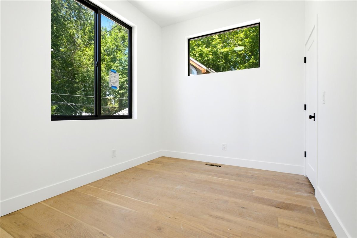 Bright interior space featuring light wood-finish flooring, crisp white walls, and contemporary black-framed windows