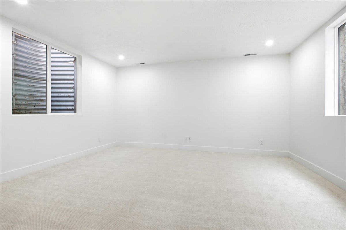 Spacious room featuring light-toned carpeting, crisp white walls, recessed ceiling lighting, and two egress windows