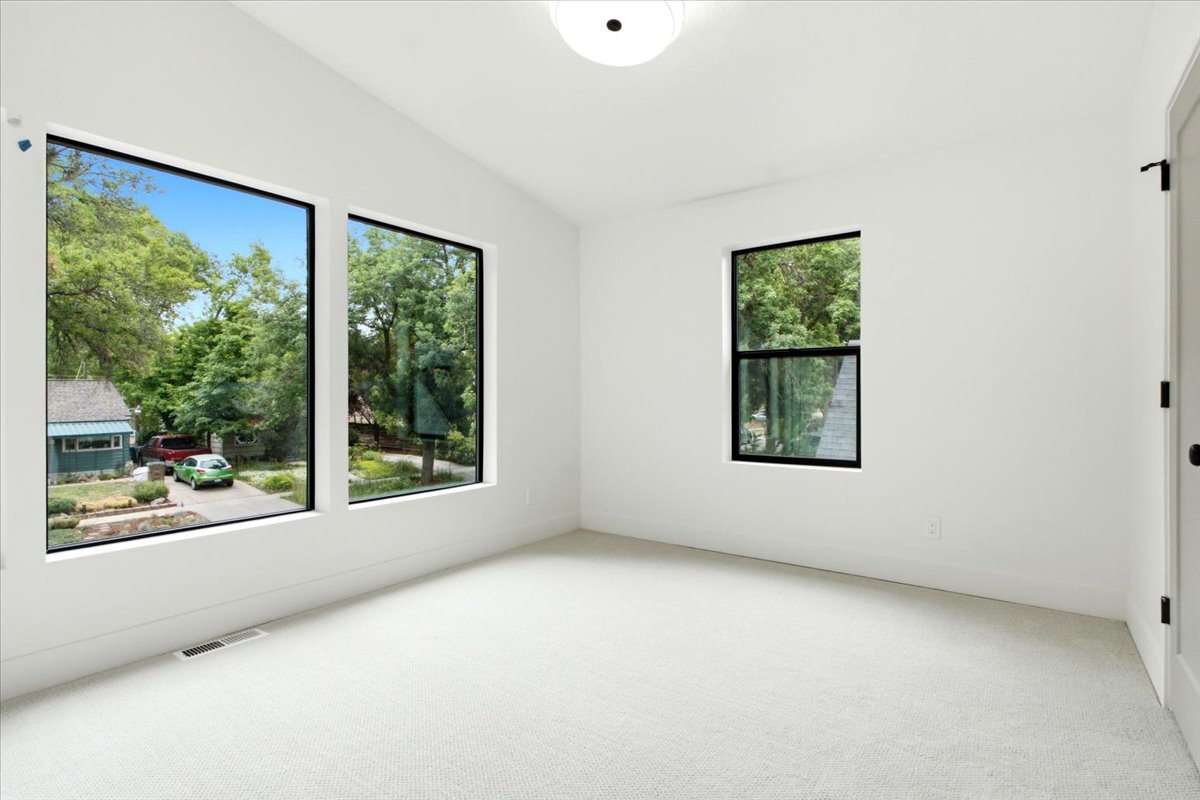 Bright interior space featuring three black-framed windows, white walls, and light-colored carpet