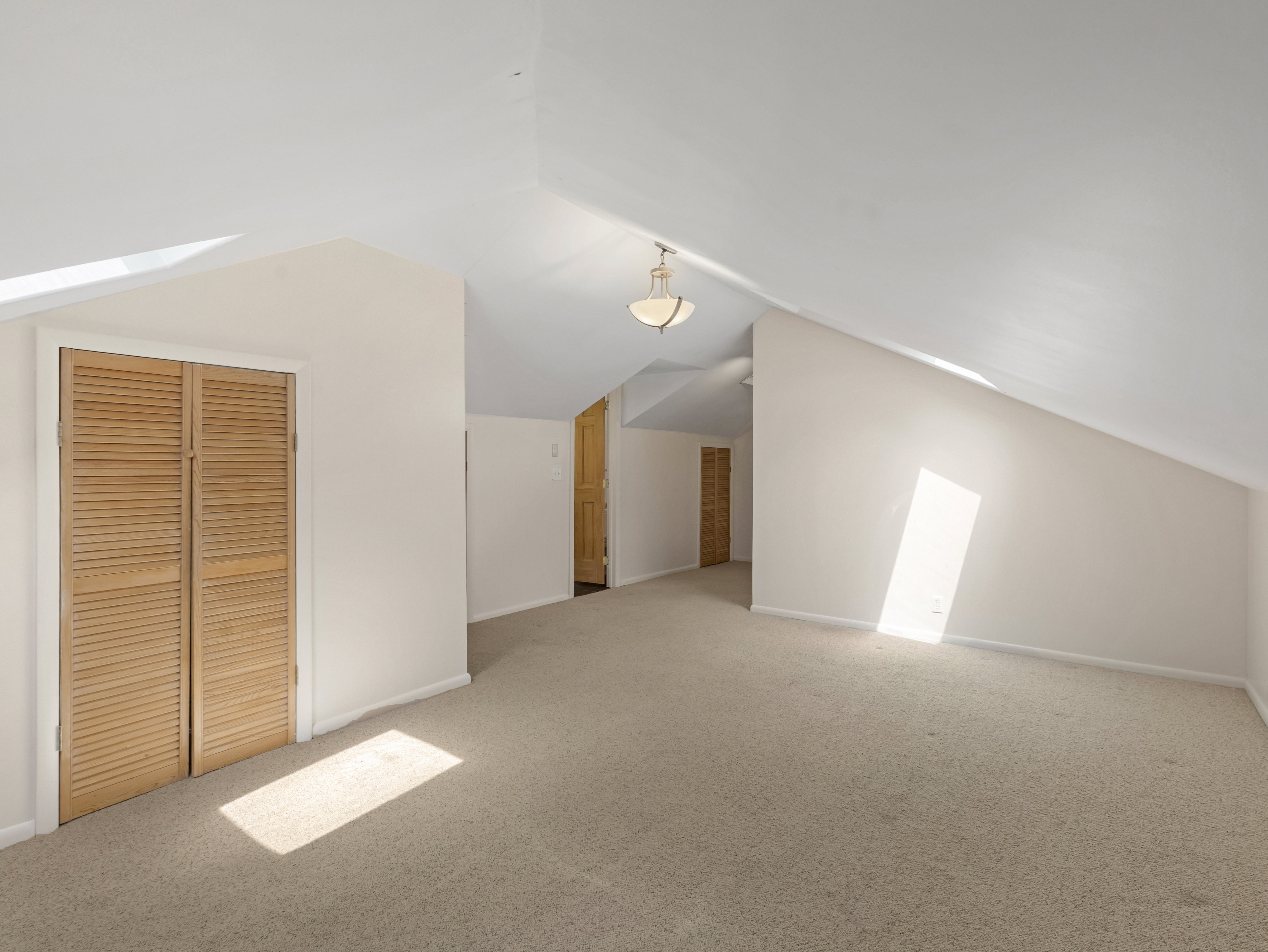 Spacious room featuring vaulted ceilings, neutral carpeting, and a built-in louvered closet