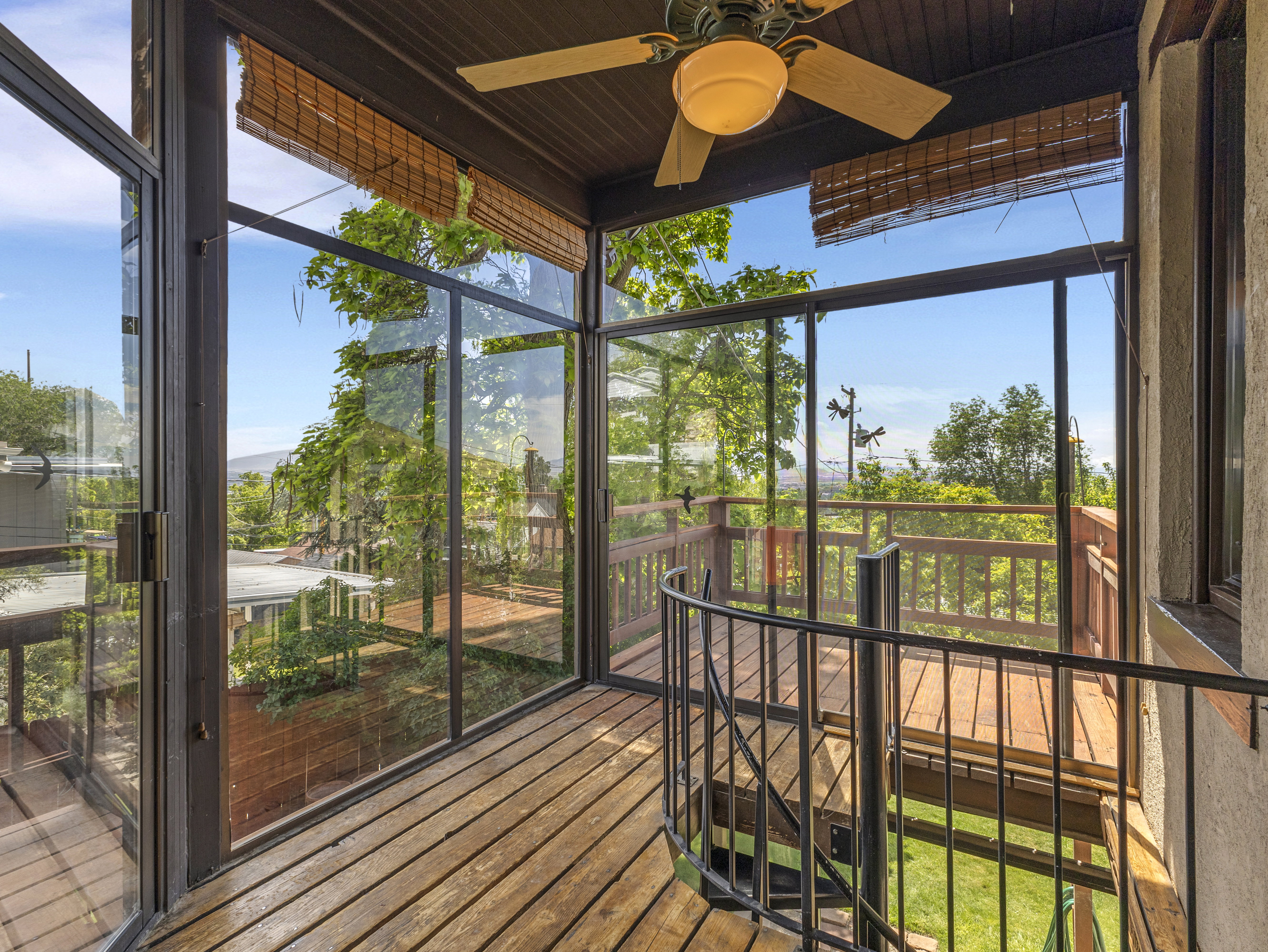 Enclosed sunroom featuring wood-finish flooring, full-height glass panels, a ceiling fan, and a spiral staircase with iron railings leading to an outdoor deck