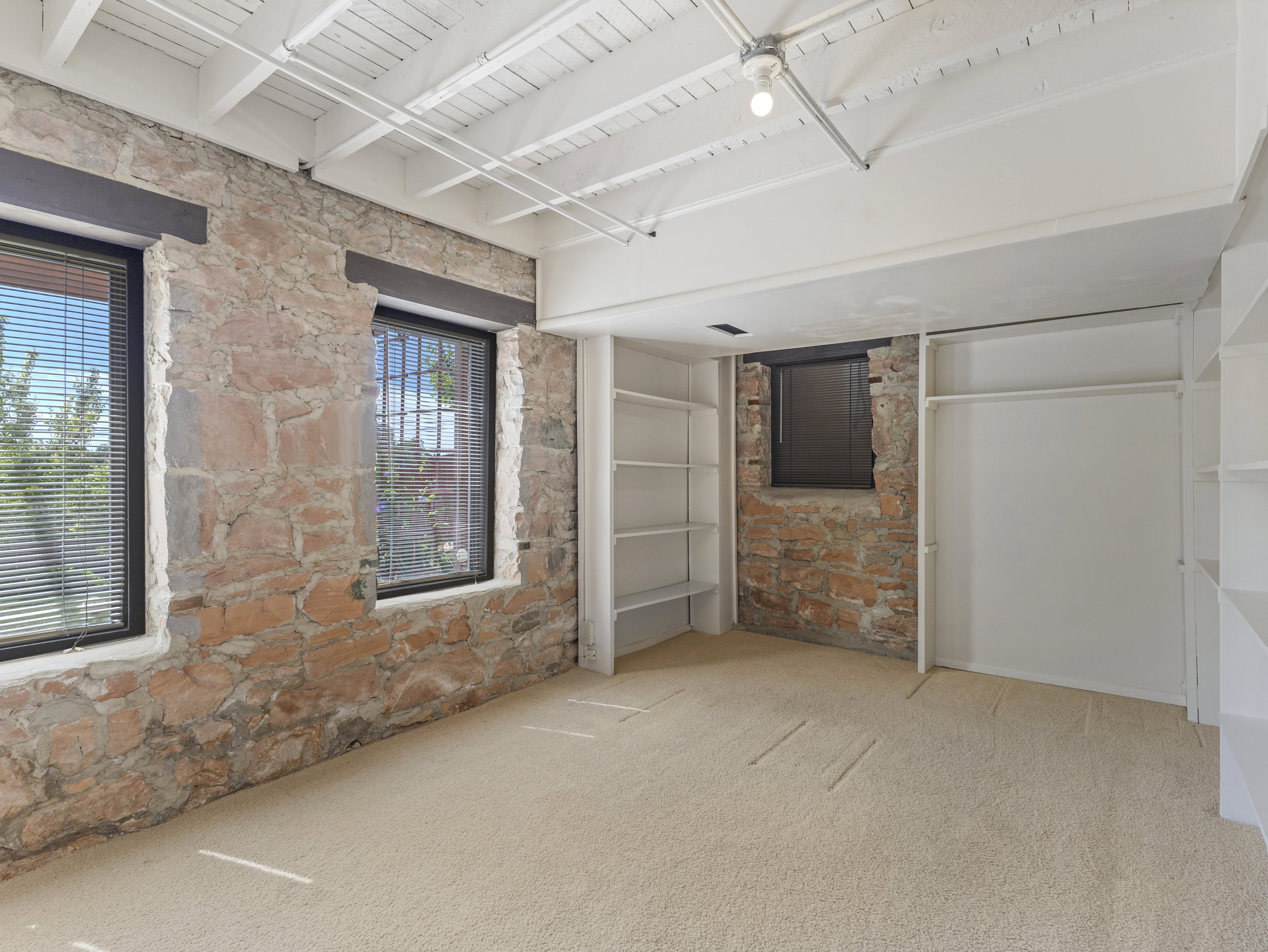 Exposed stone wall with two windows, complemented by white painted ceiling beams
