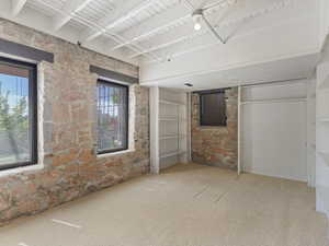 Exposed stone wall with two windows, complemented by white painted ceiling beams