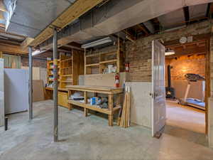 Unfinished basement space featuring exposed brick walls, concrete flooring, and extensive built-in shelving