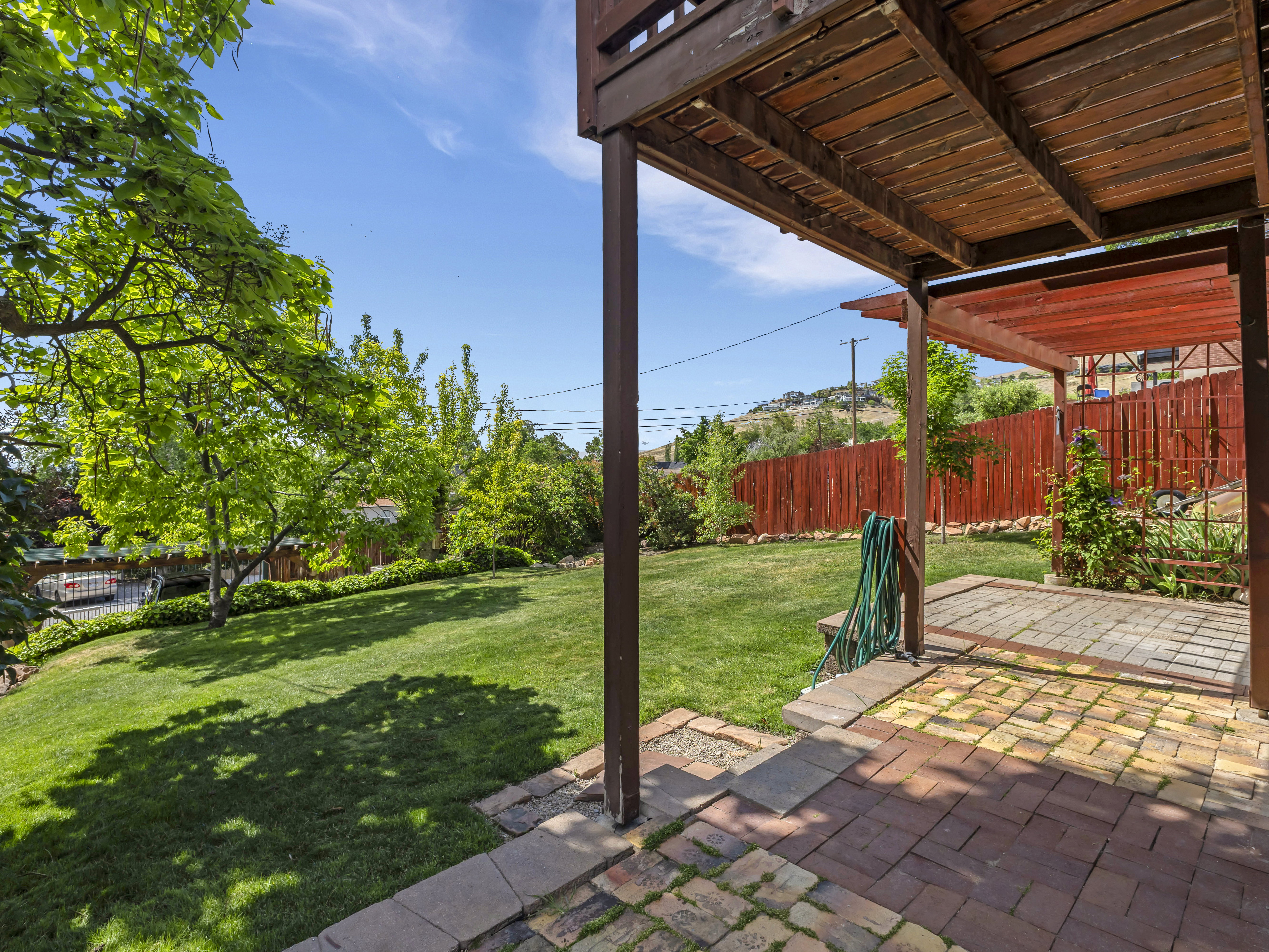 Expansive backyard featuring a brick patio, a wooden pergola, lush green lawn, mature trees, and a privacy fence