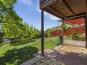 Expansive backyard featuring a brick patio, a wooden pergola, lush green lawn, mature trees, and a privacy fence