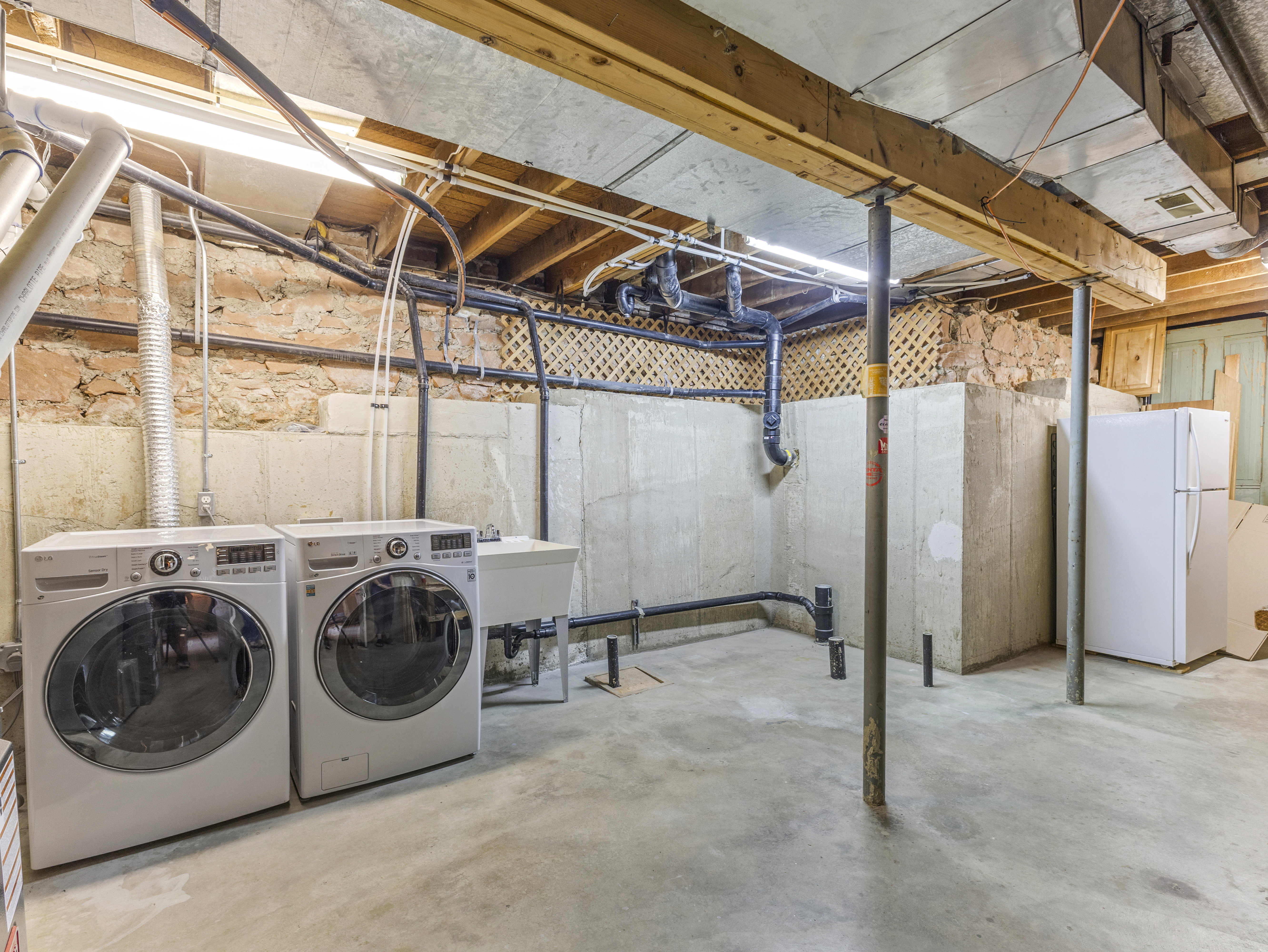 Laundry area featuring a utility sink, concrete flooring, exposed joists, and a partial stone foundation