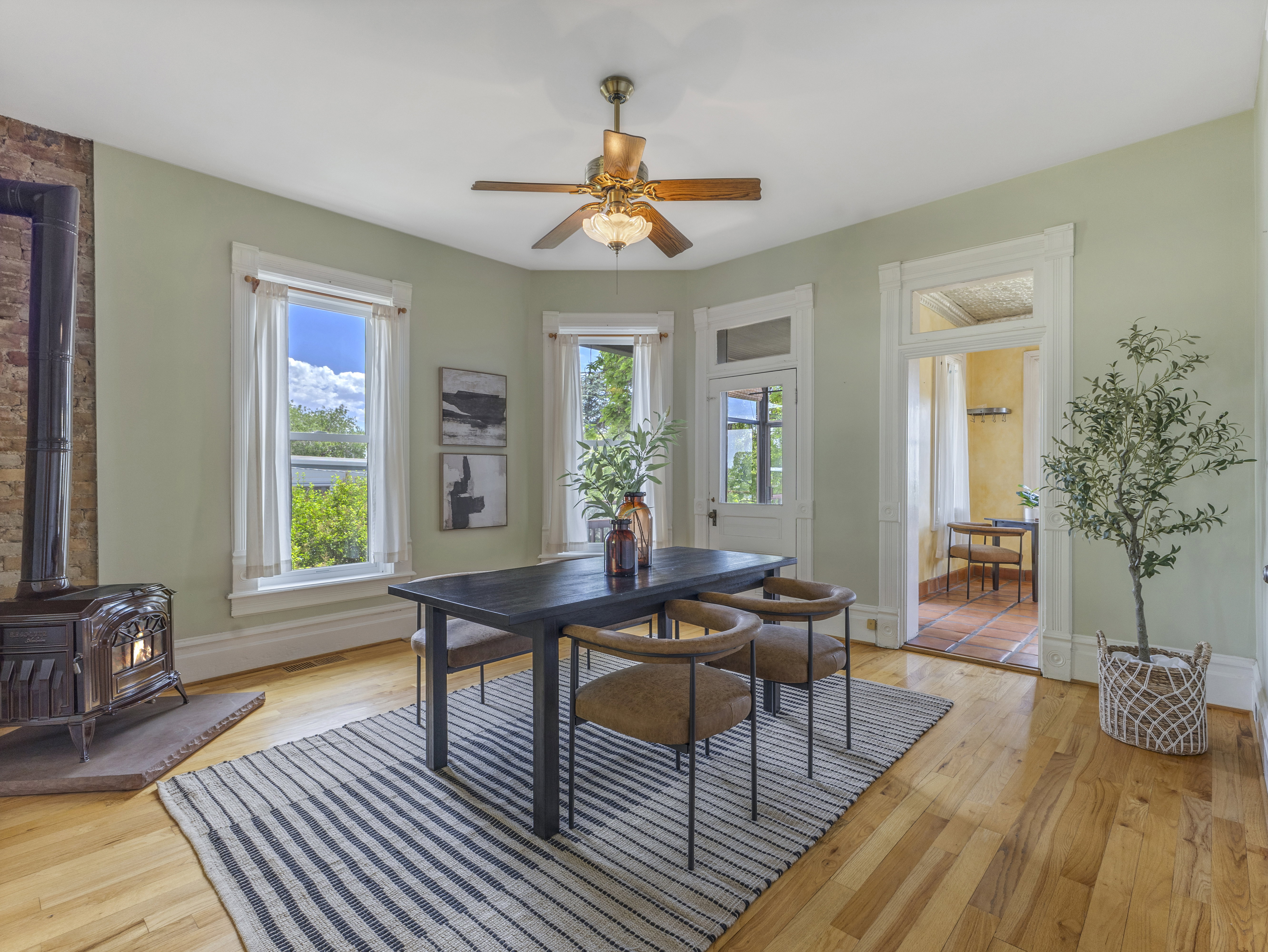 Dining area featuring wood-finish flooring, a cast iron stove with brick surround, and multiple windows