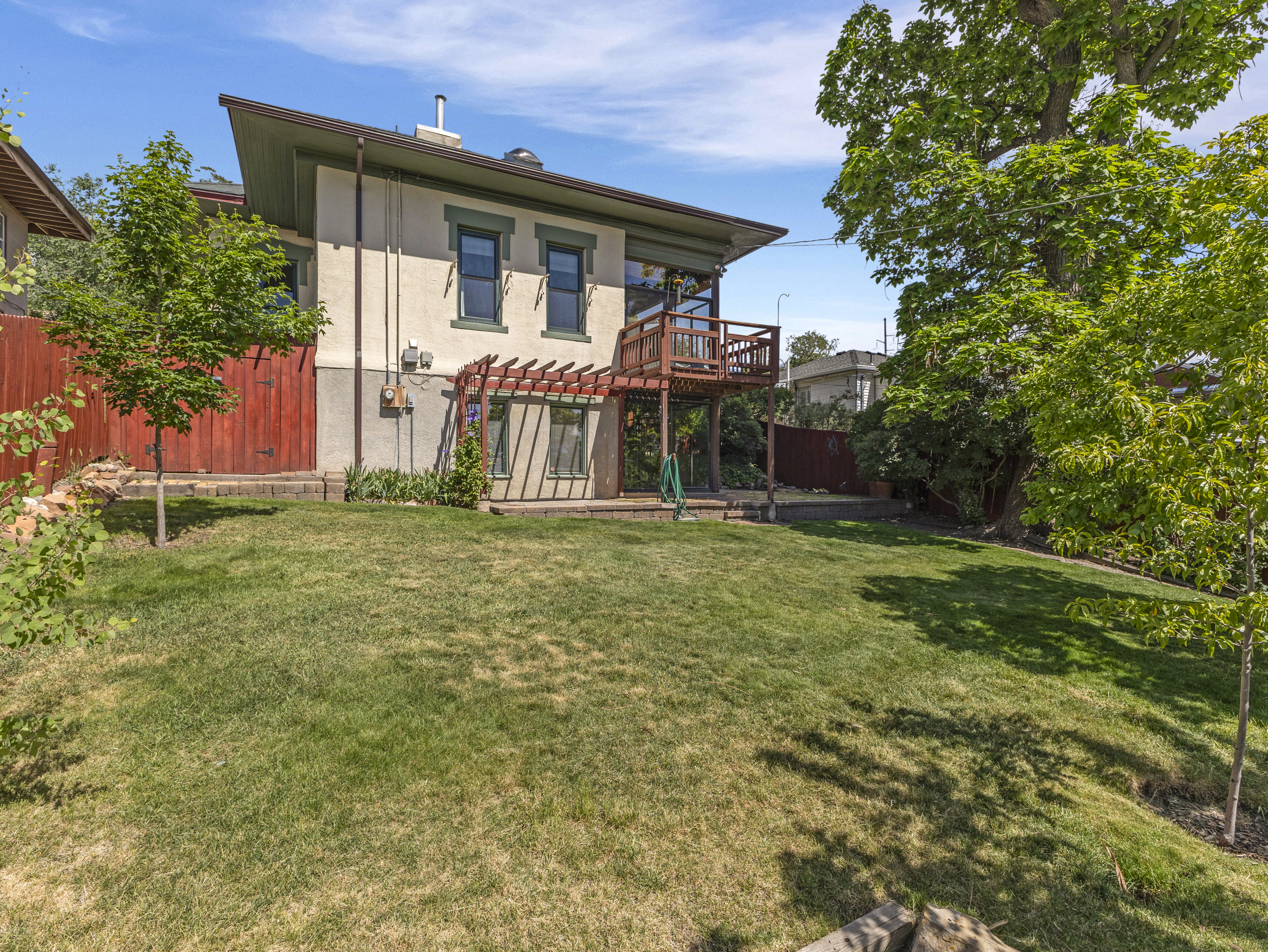 Spacious rear yard featuring an expansive lawn, mature perimeter trees, a multi-level deck, and a ground-level patio with a wooden pergola