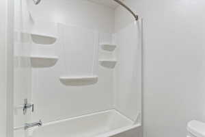 White bathtub with integrated wall panels featuring multiple built-in shelving units and a chrome shower head and faucet