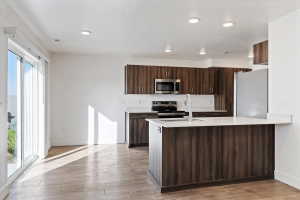 Open-concept kitchen featuring wood-grain cabinetry, stainless steel appliances, and a central island with a breakfast bar
