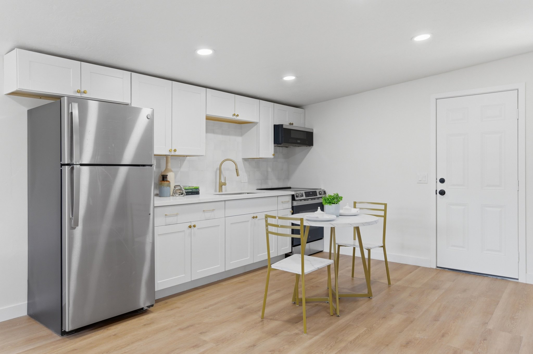 Sleek kitchen featuring white cabinetry, stainless steel appliances, wood-finish flooring, recessed lighting, and a paneled entry door