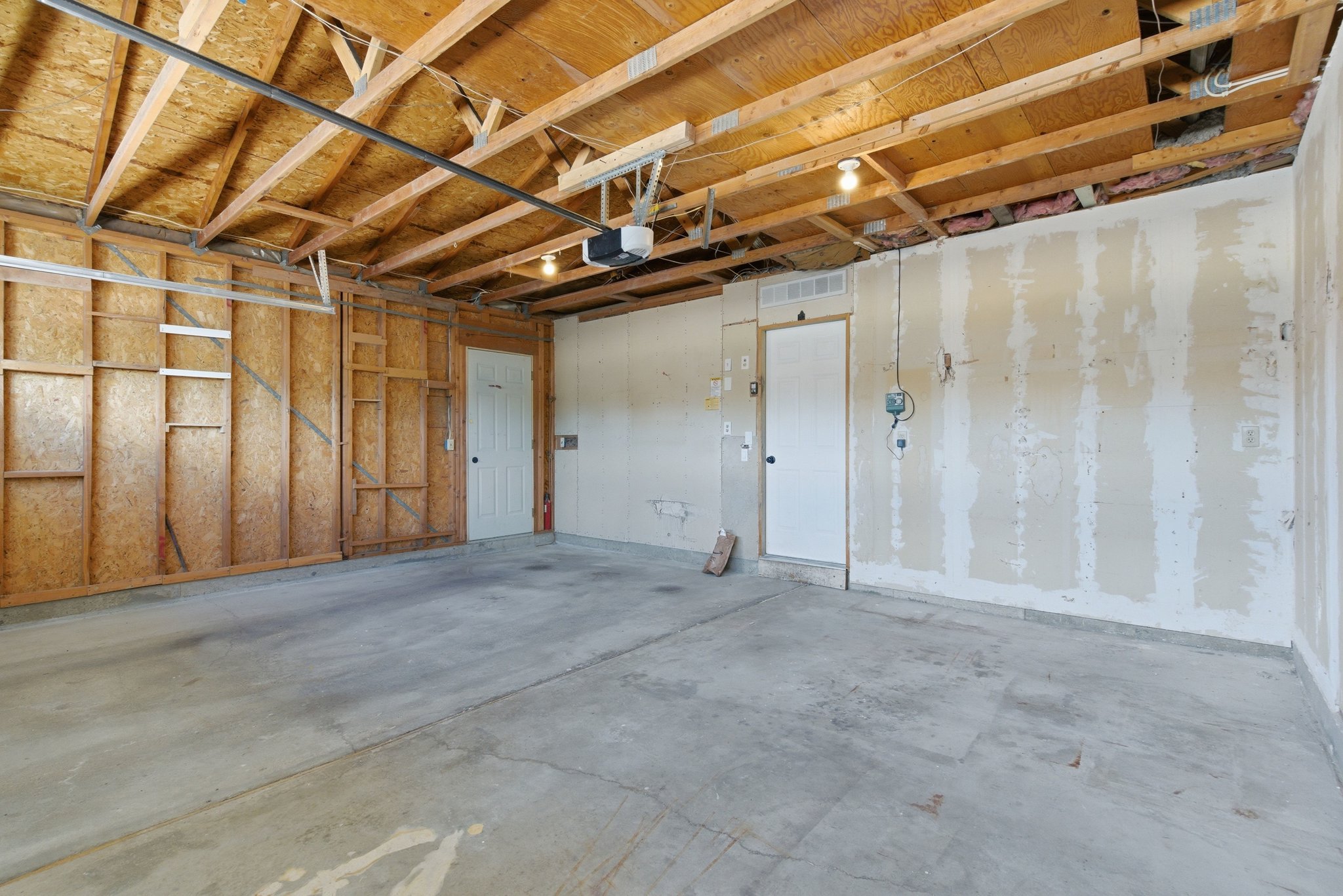 Spacious two-car garage featuring a concrete floor, exposed wood ceiling joists, and two interior access doors