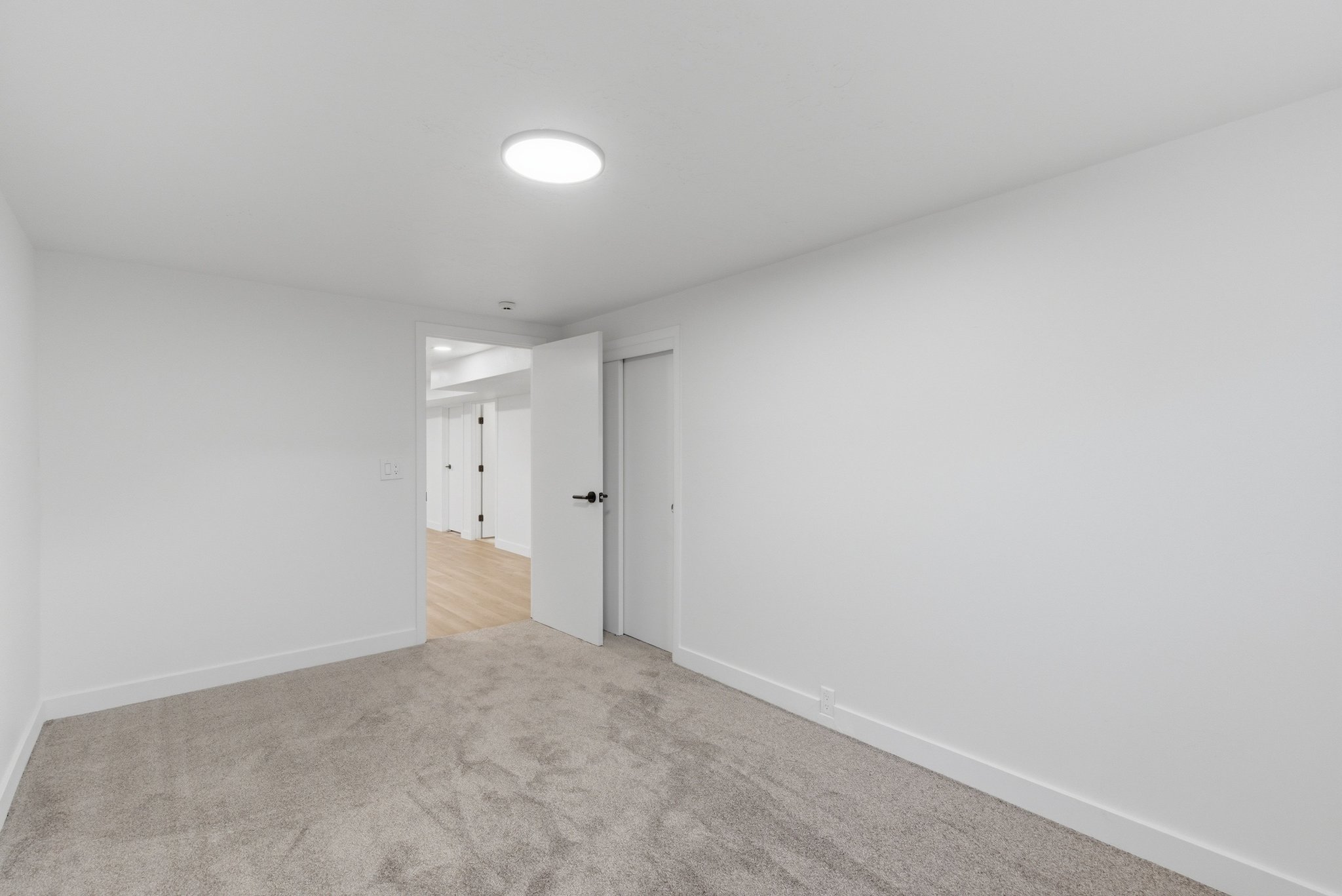 Carpeted room featuring a white door with black hardware, white baseboards, and a circular flush-mount ceiling light