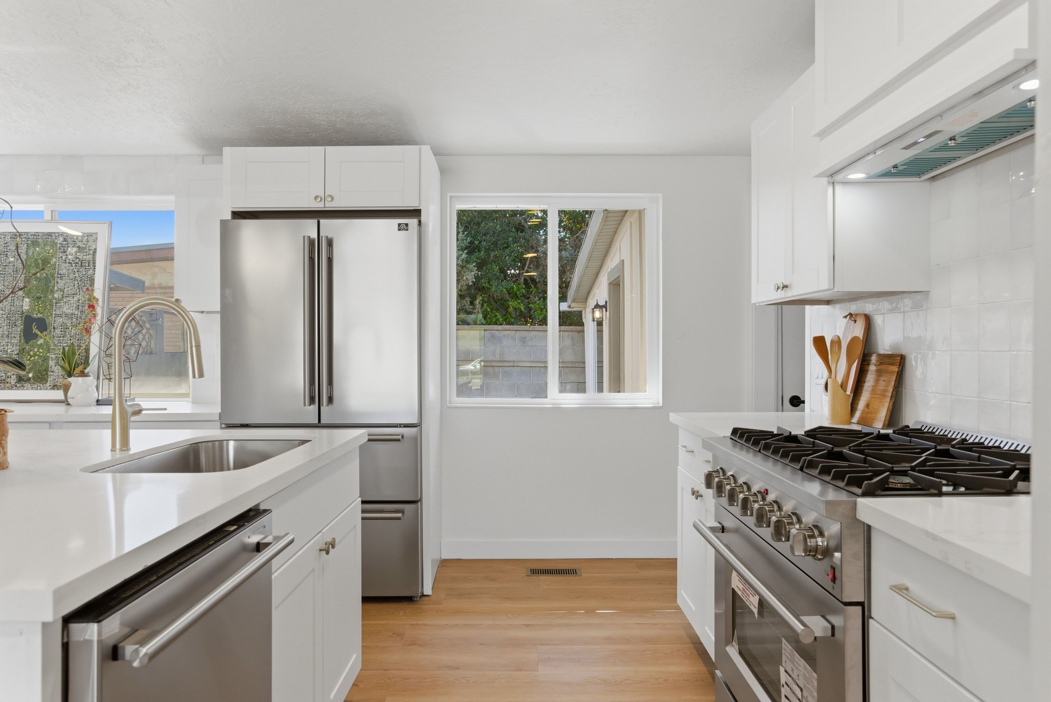 Modern kitchen featuring white cabinetry, light-toned countertops, stainless steel appliances, and wood-finish flooring