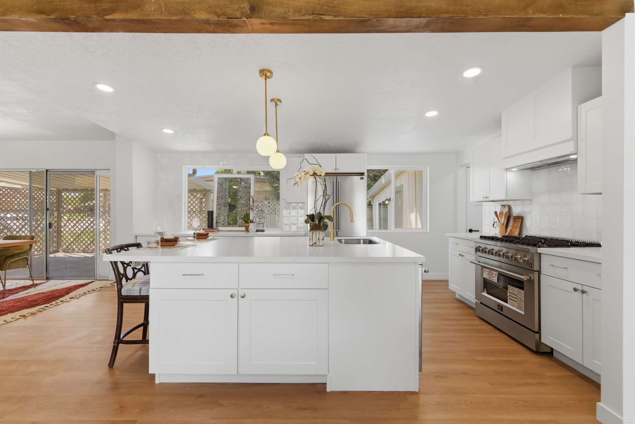 Modern kitchen featuring a large central island with seating, white shaker cabinetry, stainless steel appliances including a range with a hood, and wood-finish flooring