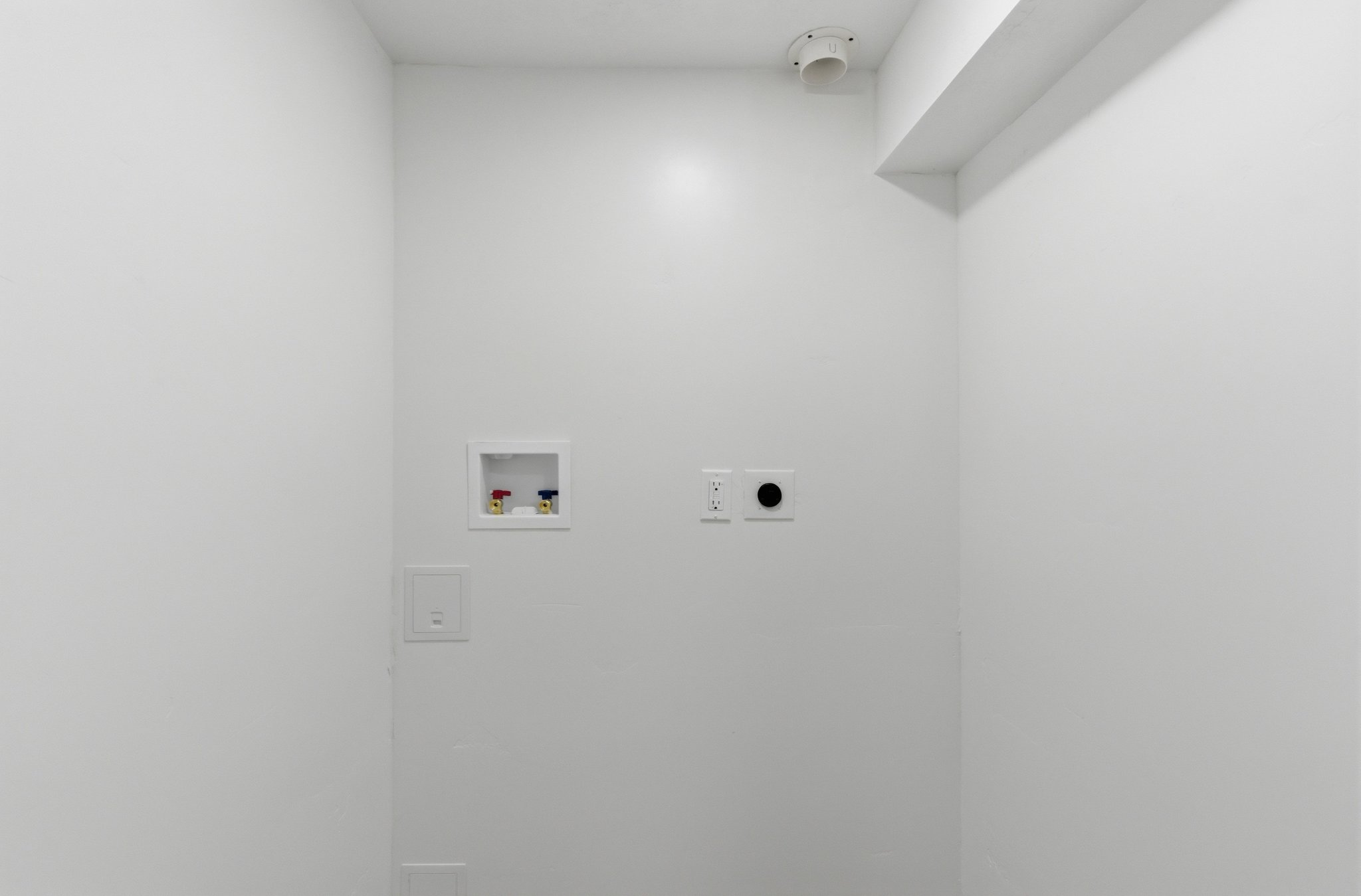 Utility area with white painted walls, featuring a water hookup box, electrical outlets, and a dryer vent