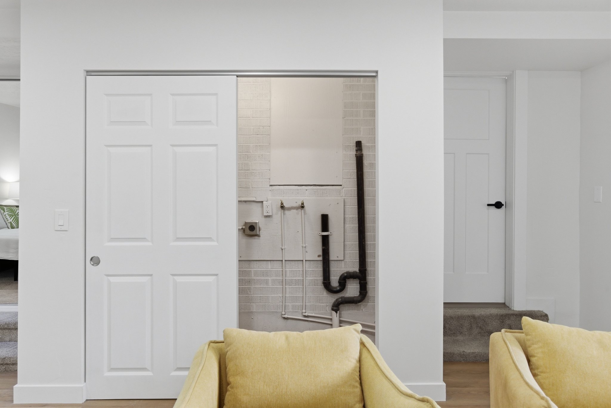 Utility closet with white sliding six-panel door, light brick-patterned tile wall, and exposed piping