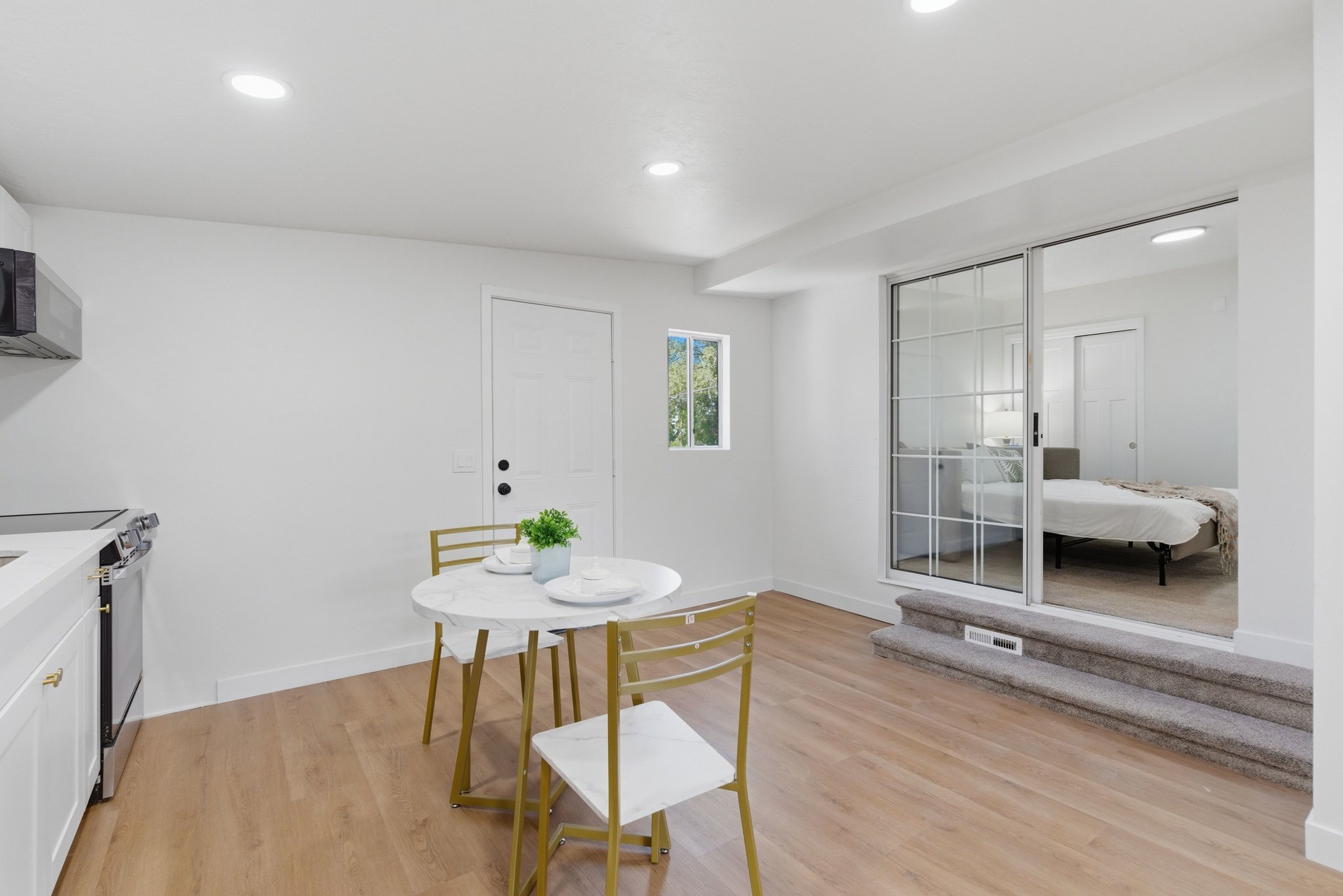Open-concept living space with wood-finish flooring, recessed lighting, and a white kitchen featuring a stainless steel range and microwave