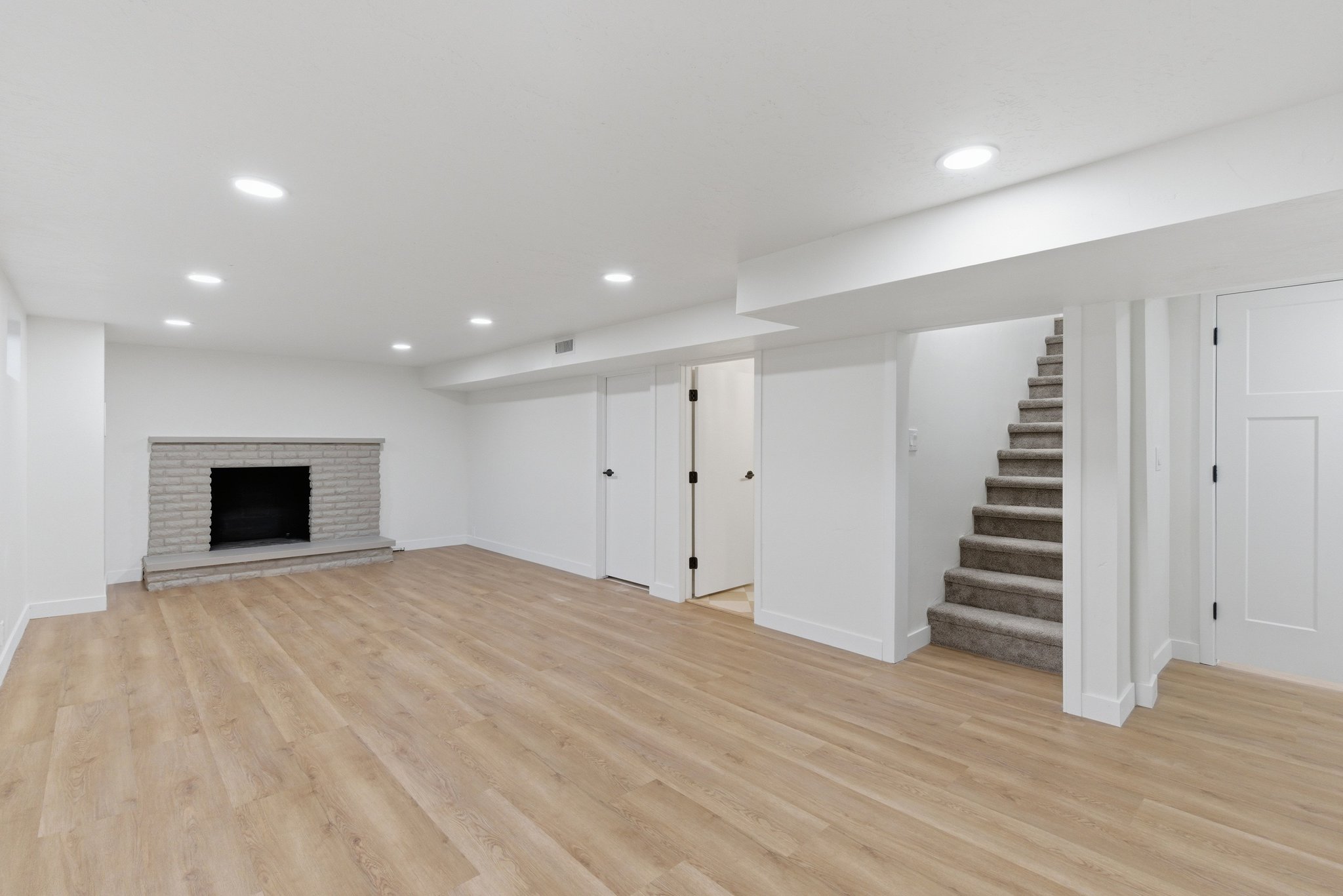 Spacious room featuring wood-finish flooring, a light gray brick fireplace, recessed lighting, and a carpeted staircase