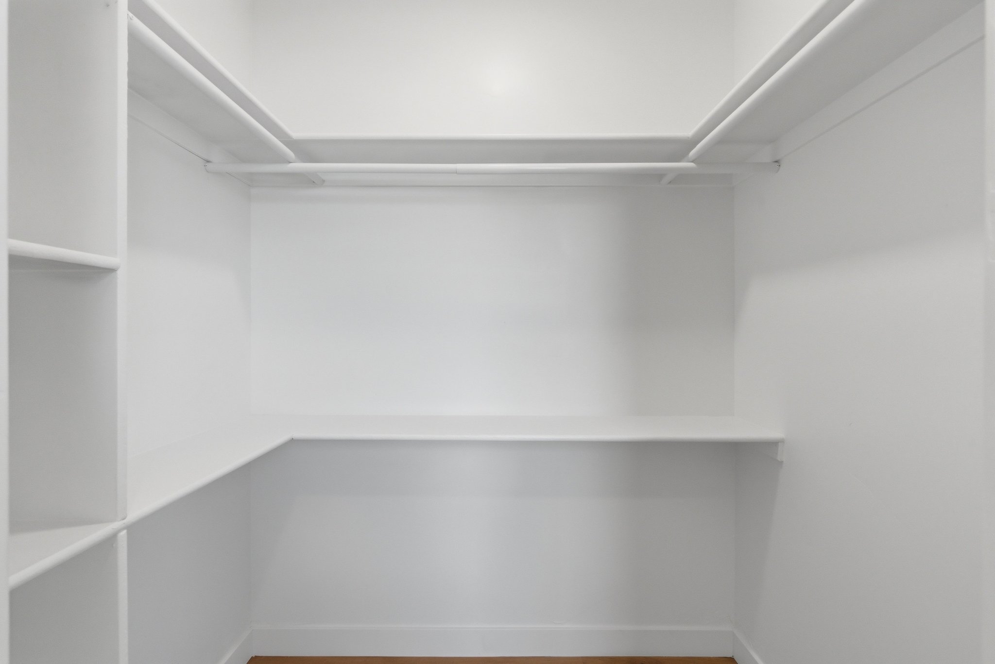 Walk-in closet featuring white built-in shelving, hanging rods, and wood-finish flooring