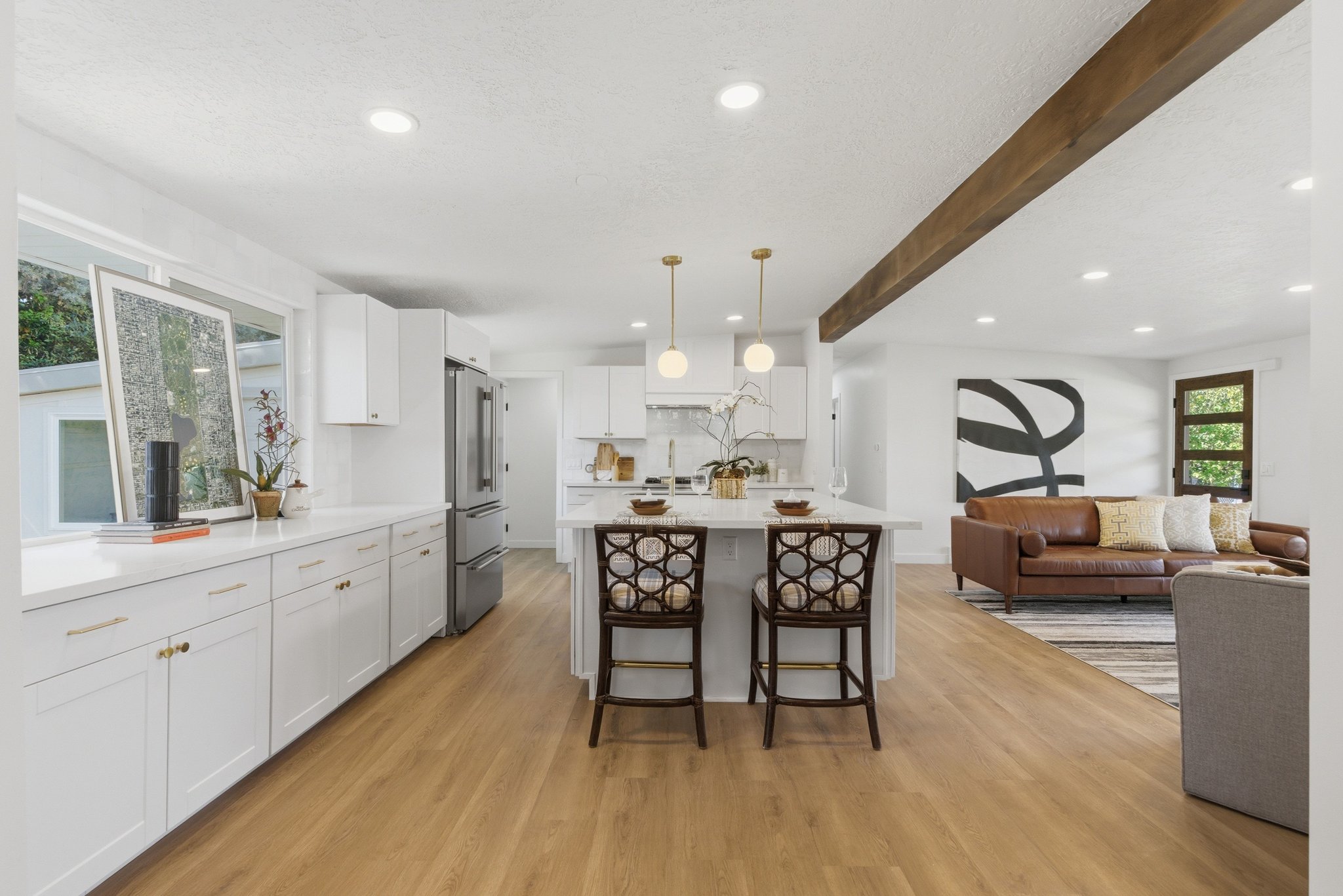 Open-concept kitchen featuring an island with pendant lighting, white cabinetry, integrated stainless steel appliances, and wood-finish flooring throughout